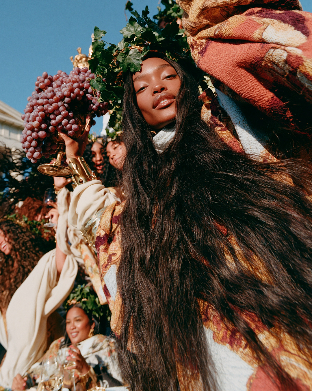 A guest in a vine crown holding grapes, laughing among friends